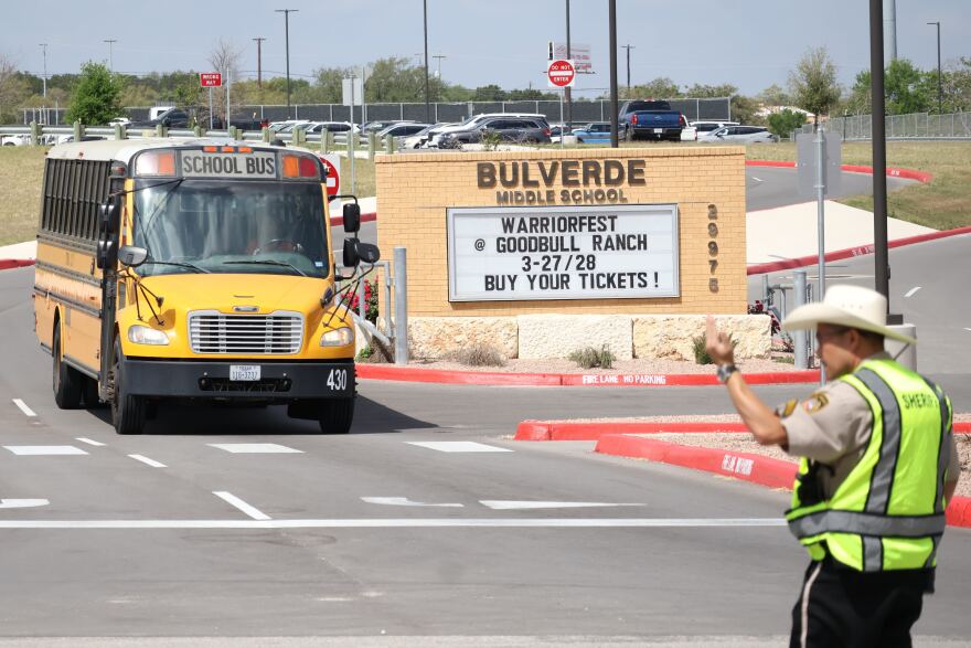 A school bus approaches a sheriff deputy at Bulverde Middle School on Monday, March 30, 2026. Students at Hill Country College Preparatory High School were evacuated to the middle school Monday after one of their classmates shot and injured a teacher. The student then turned the gun on himself and died on the scene, according to law enforcement.