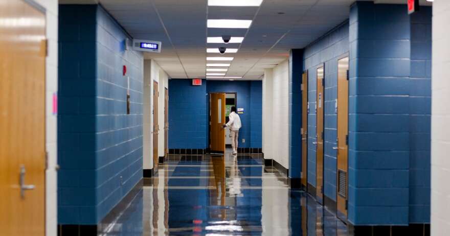 A student walks in a school hallway that is otherwise empty.