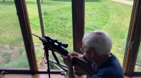 Dave Clausen, a retired veterinarian in Amery, Wisconsin, poses with his rifle in his living room window. “Sometimes I go out to start the coffee and I'll take a quick look out the window,” Clausen said. If he sees a deer, he shoots. He’s able to do so because of nuisance permits, which allow him to harvest white-tailed deer outside of Wisconsin’s hunting season. (credit: Ellie Katz / Points North)