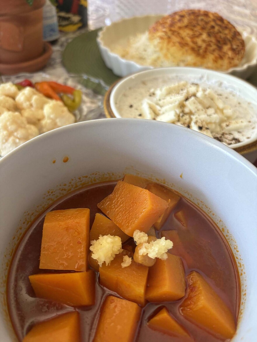 bowl with cut pieces of orange squash and garlic sprinkled on top. dishes with rice, vegetables and a yogurt and cheese dish in the background