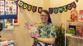 Amara Vear, founder of Queer Comics Peddler holds a comic up at their pop-up shop.