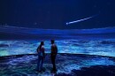 Man and woman stand inside museum 360 project with ocean covering them 
