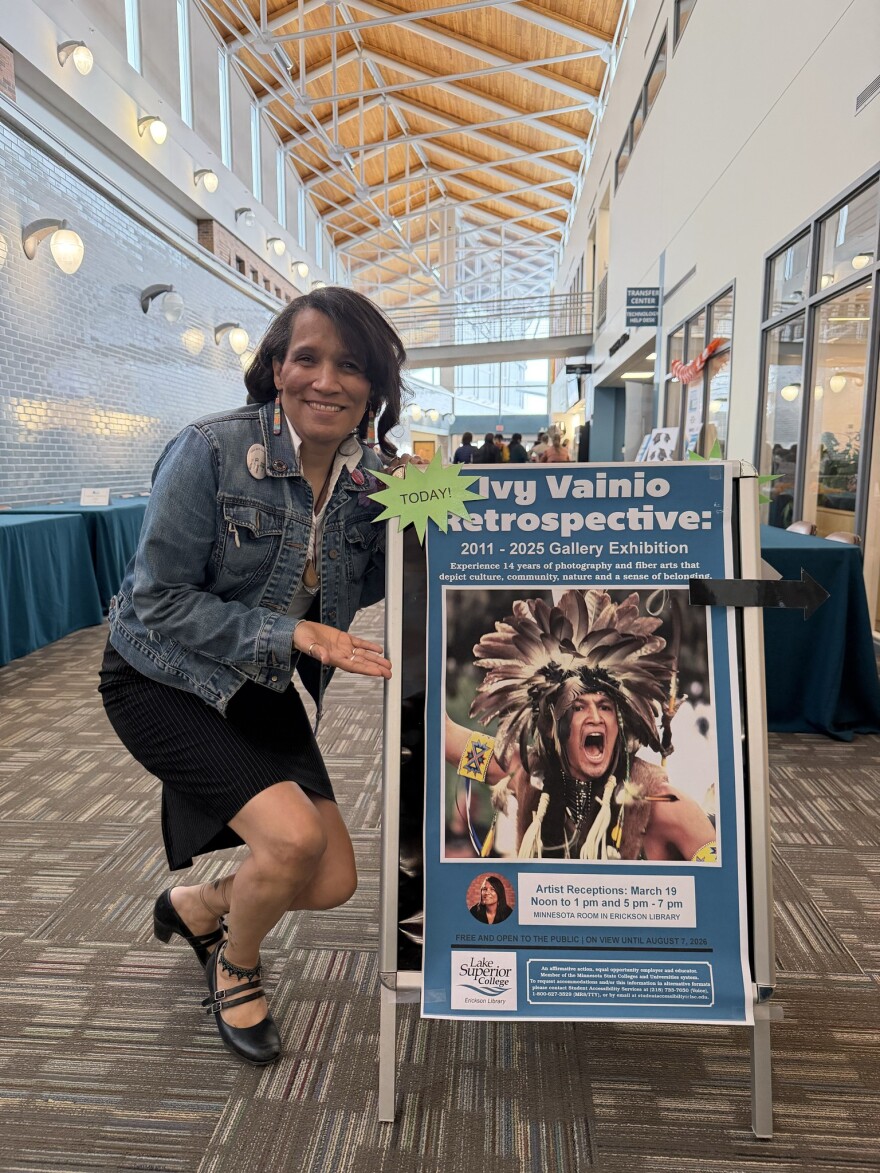 Interior image of a woman standing by a sandwich board promoting an art exhibit
