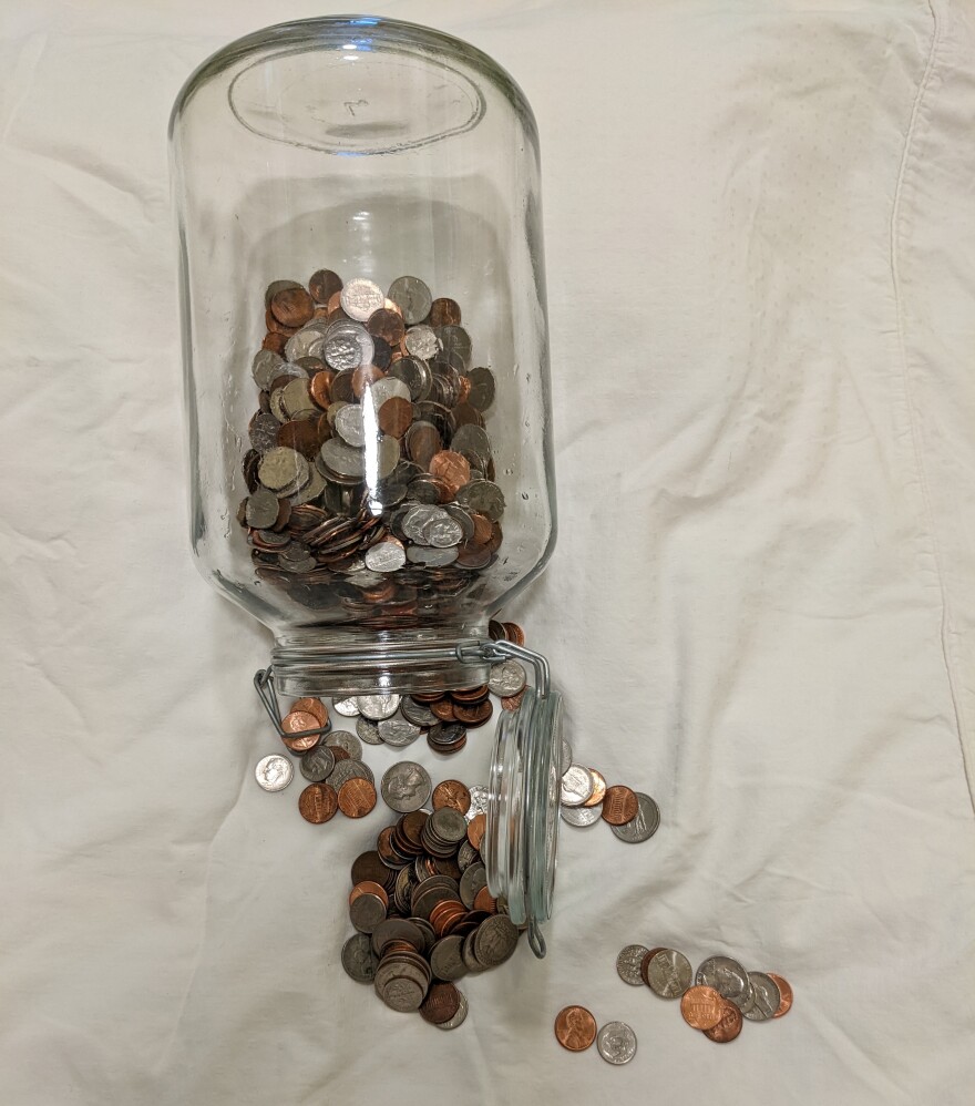 A glass jar with coins spilling out of it.