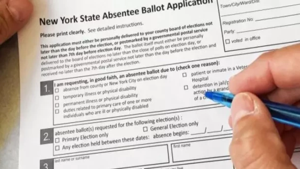 A person fills out a New York State absentee ballot application with a blue pen.