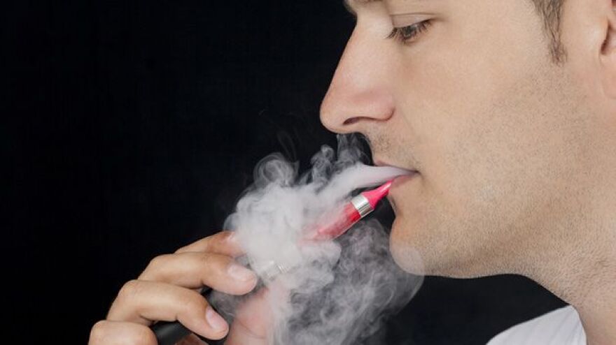 Man using an e-cigarette with vapor swirling around his face.
