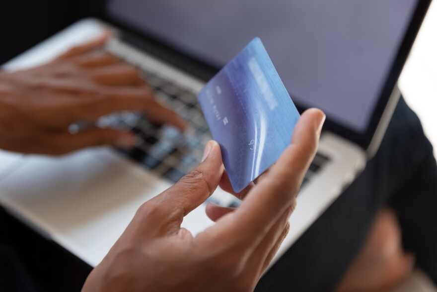 Close up of woman's hand holding a blue credit or debit card. In the background is her laptop.