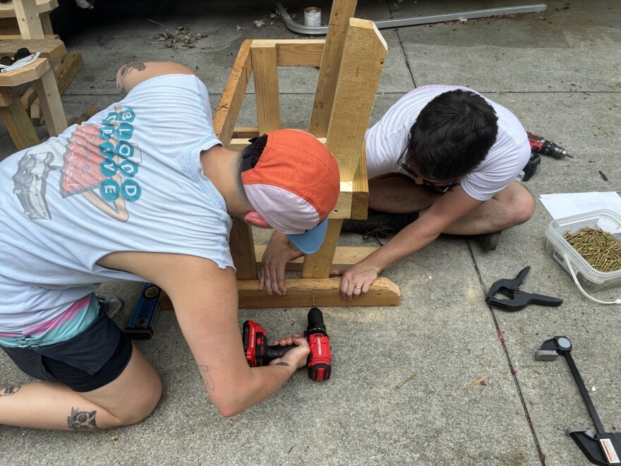 Ash Pancost drills a screw into a park bench while David Braga holds the board in place.