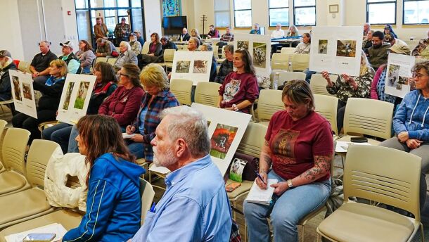 Matanuska-Susitna Borough residents hold signs during an April 21, 2026, Borough Assembly meeting displaying photos of some of the 25 dogs found dead last week at a kennel near Willow.