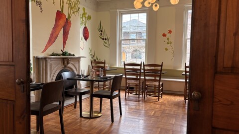 Two open doors frame a dining room with wooden floors, a fireplace, and vegetables painted on the walls.