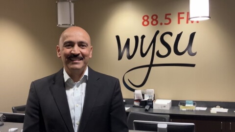 Juan Santiago facing the camera smiling with the words "88.5 FM WYSU" behind him on the wall