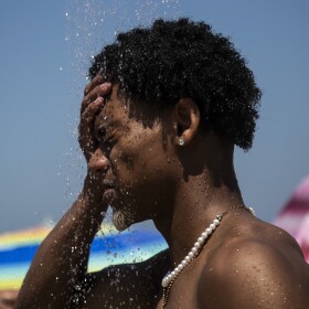 man standing on a beach splashing water on his face