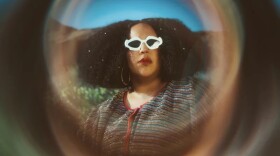 A woman wearing sunglasses looks at the camera with rolling hills in the background and a blurred effect surrounding her face.