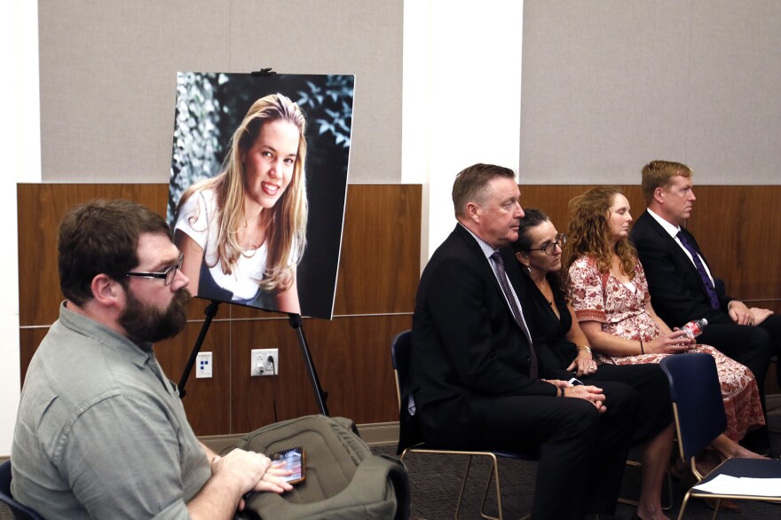 Chris Lambert, documentary podcaster, sits in front of a poster of Kristin Smart with family members nearby hours after a jury found Paul Flores guilty of the 1996 murder of Cal Poly student Kristin Smart on Oct. 18, 2022 in Salinas, Calif.