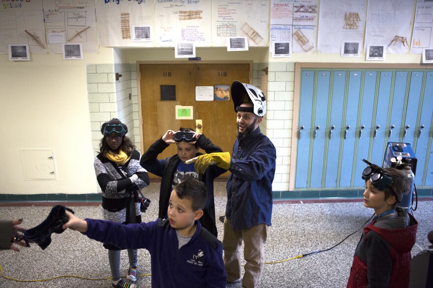 Mr. Guarraia and students wear protective gear before welding part of the sculpture's frame in a hallway at Arbutus Middle School.
