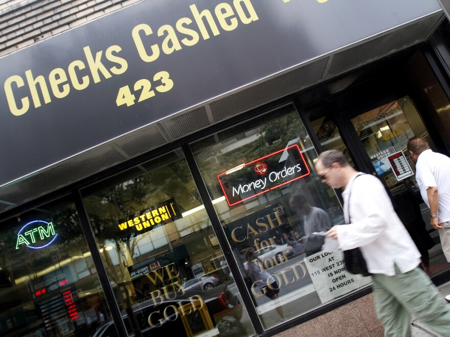 Photo of a Checks Cashed storefront and man walking in front of it on the sidewalk.