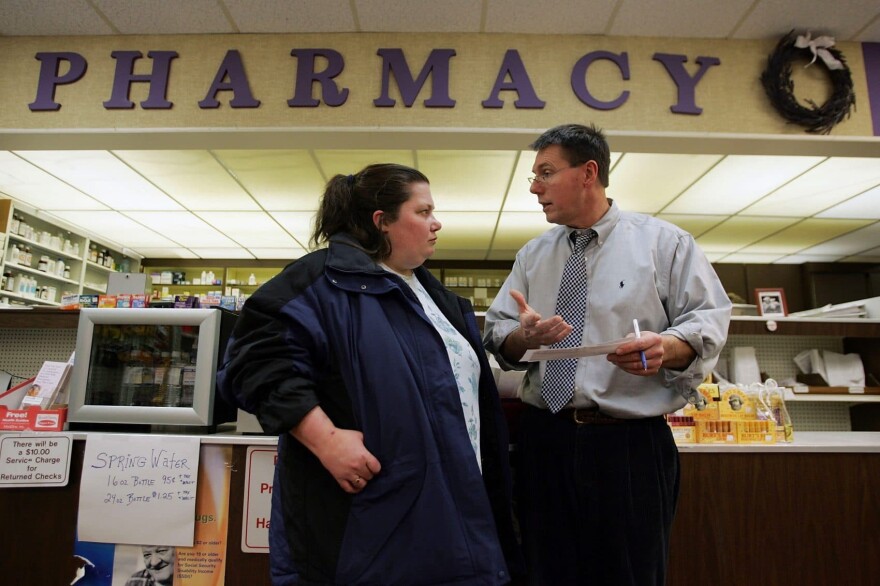 In this Jan. 18, 2006 photo, pharmacist, William Hewitt, (right) speaks with Rebecca Allen about her Medicare prescription drug benefit program as she buys her drugs at Rosemont Pharmacy in Portland, Maine. (Joe Raedle/Getty Images)