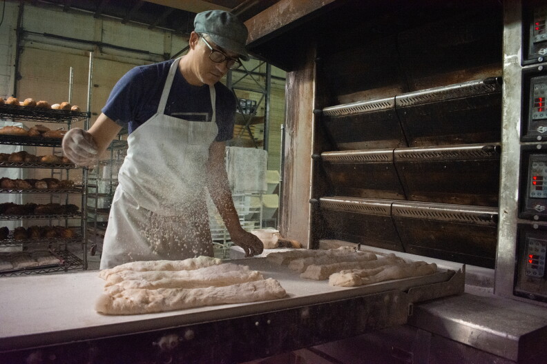 Baker dusting loaves of bread with flour