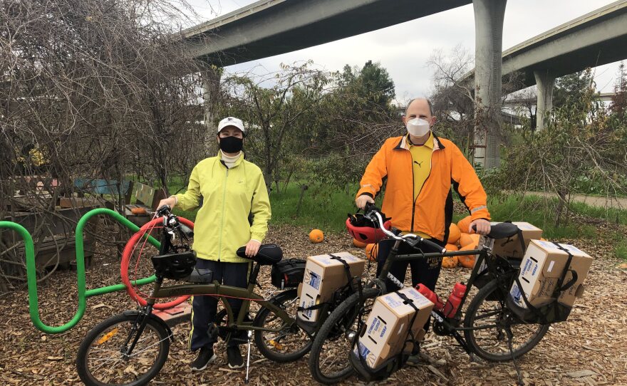 Image 1: Miki and Jon in brightly colored jackets posed with their bikes, produce boxes strapped and ready to go. Image 2: Cream and black toned rooster standing near a metal fence. Image 3: Hand-painted wooden Veggielution directional sign. 