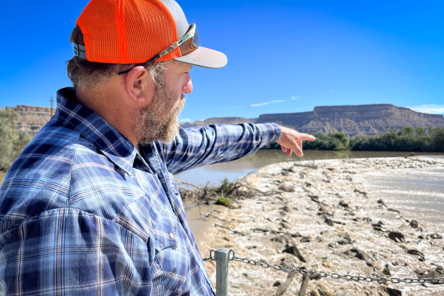 Coby Hunt points across the dam that diverts water from the Green River into the irrigation canal that runs by his field, Aug. 19, 2024. Because he’s been paid to fallow that land, the water he would typically use on his crops has been returning to the Green River downstream.