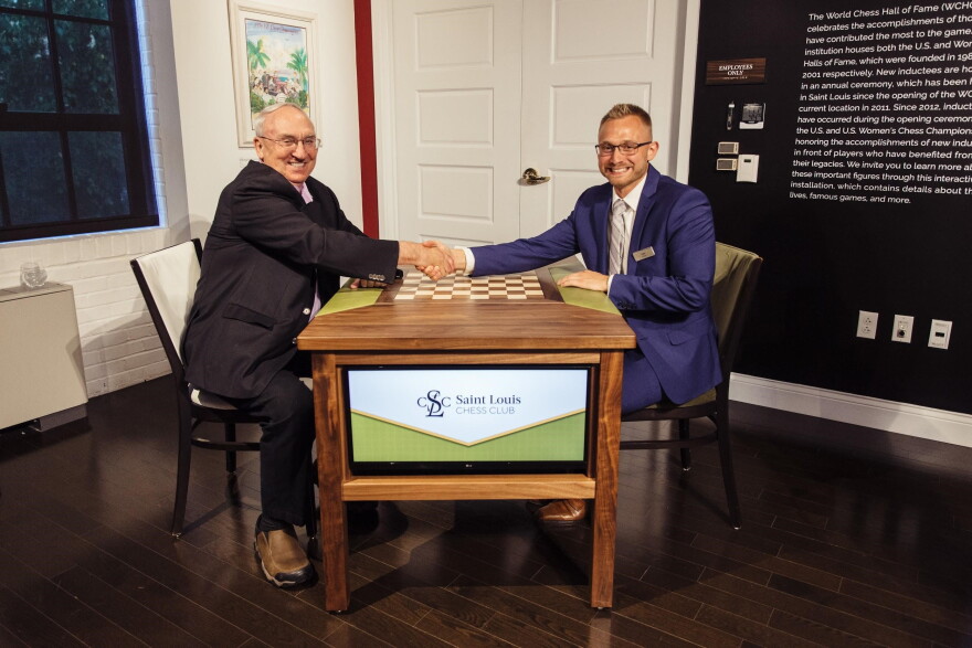 St. Louis Chess Club co-founder Rex Sinquefield (left) shakes hand with Nate Cohen across a "Sinquefield Table."