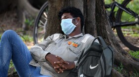 A man wearing a face mask and a tag that reads "Safety starts with me" takes a nap in Singapore on April 15, 2020. (Roslan Rahman/AFP/Getty Images)