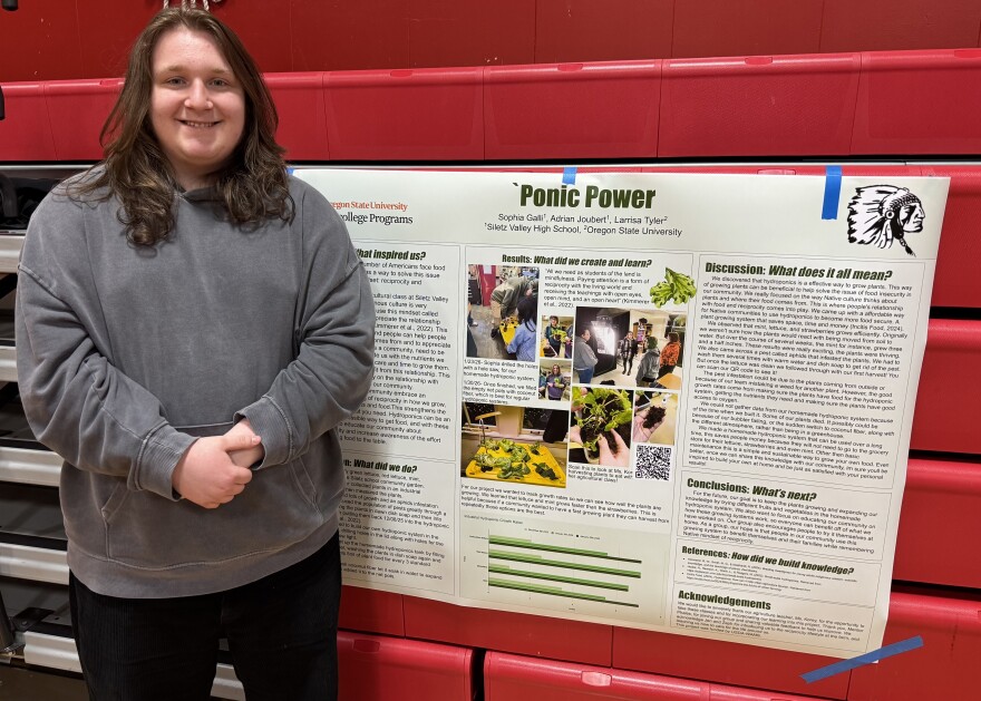 Teenager stands in front of a research poster about hydroponics.