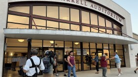 Uvalde residents walk outside and greet each other after a forum with school district leadership as camera crews look on.