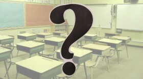 Image of classroom desks; a large question mark in the foreground 