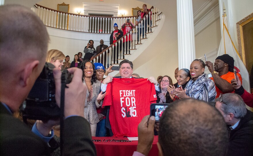 Gov. JB Pritzker holds a shirt commemorating the movement to raise the minimum wage to $15 after signing the bill on February 20, 2019. The wage hits $15 in 2025.