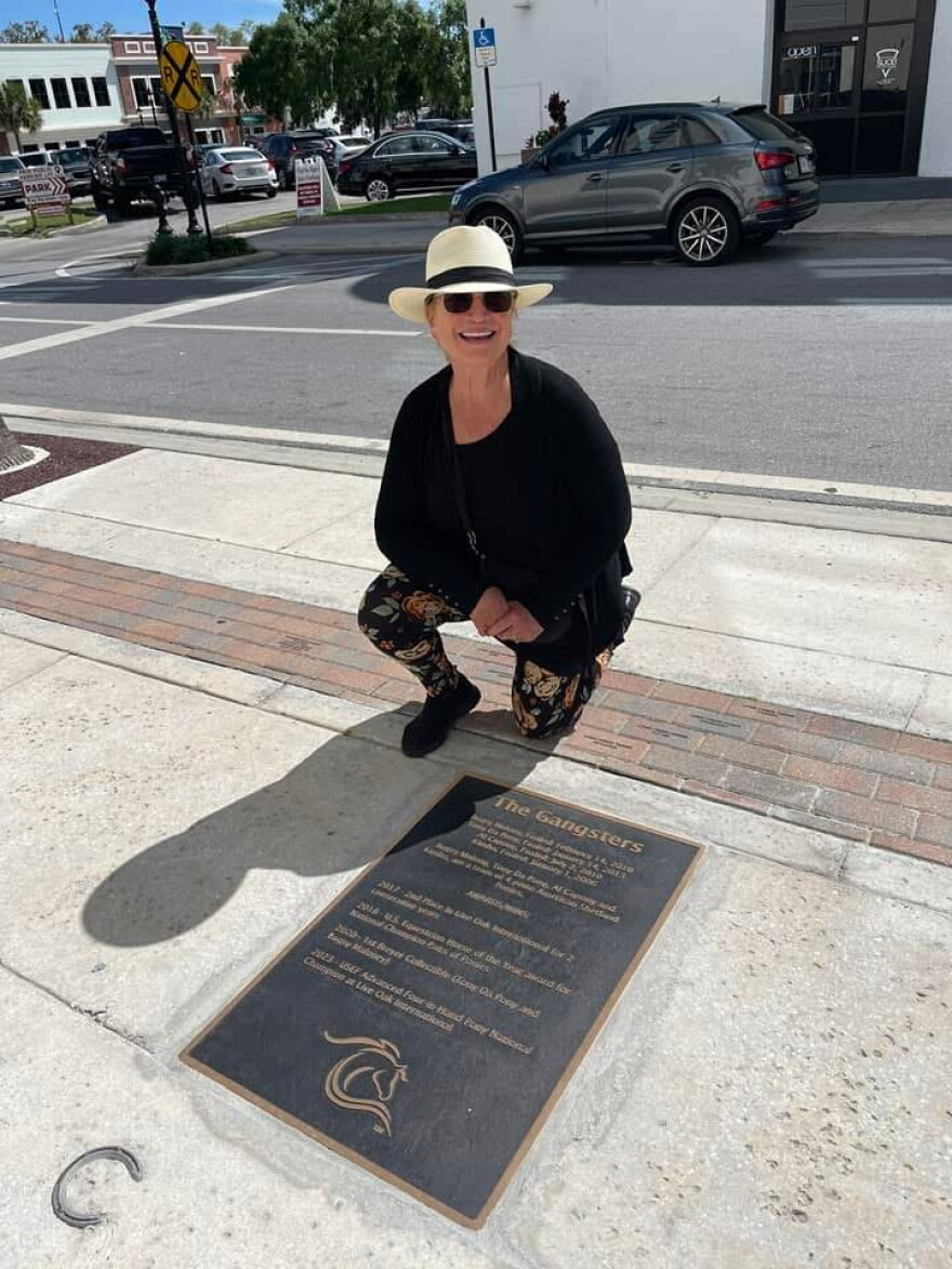 Mary Phelps poses for a photo next to a plaque in downtown Ocala commemorating her ponies.