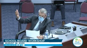 Brennan Asplen, wearing a face masks, gestures at a table