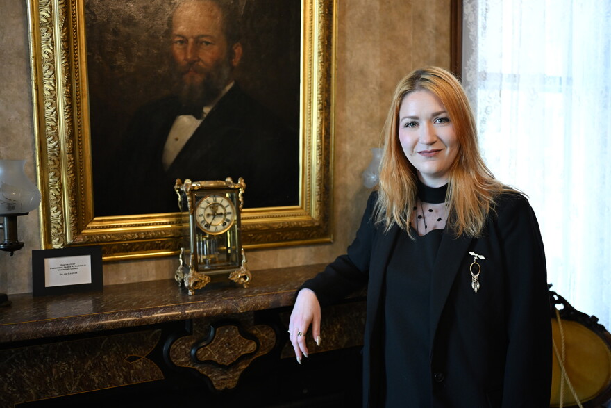 A woman in black stands in front of a presidential portrait