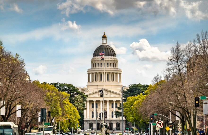 The California State Capitol rises in the center of the frame, with symmetrical rows of trees leading up to it on either side.