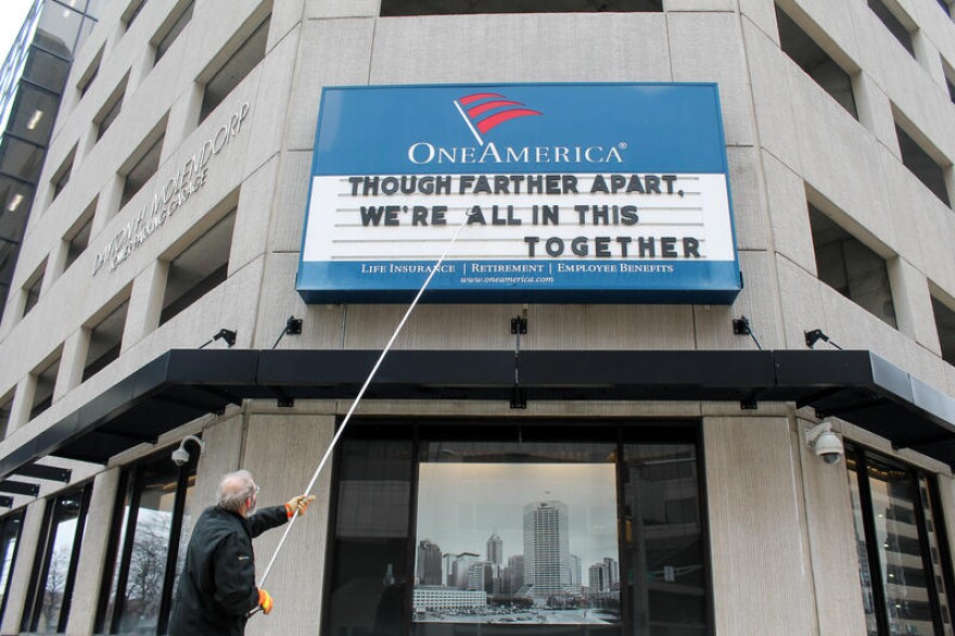 A man adjusts the One America sign in downtown Indianapolis. It usually displays a pun, but the message shortly before the governor's address reads: 'Although farther apart, we're all in this together.'