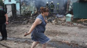 TOPSHOT - A woman walks past firefighters extinguishing a fire in a house that was damaged following a missile attack in a village outside Kyiv on August 30, 2023, amid the Russian invasion of Ukraine. (Photo by Anatolii STEPANOV / AFP) (Photo by ANATOLII STEPANOV/AFP via Getty Images)
