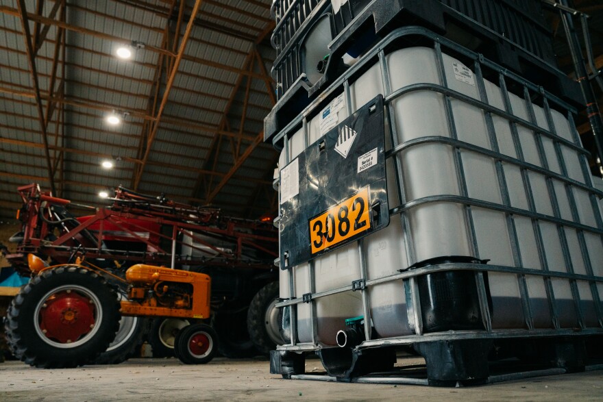 A large square gray container sits in a warehouse next to an orange tractor.