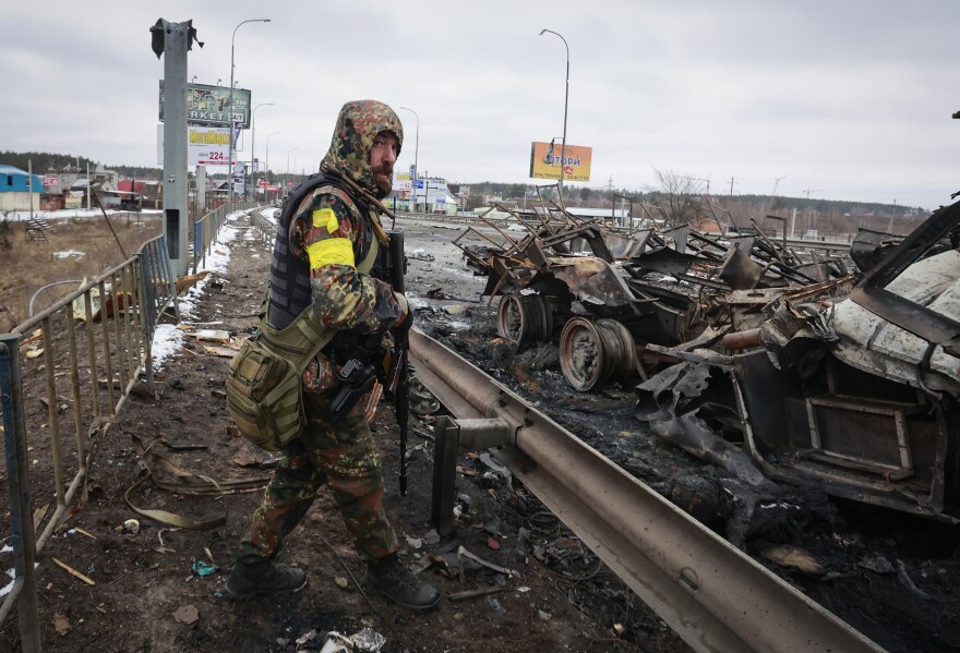 An armed man stands by the remains of a Russian military vehicle in Bucha, Ukraine, close to the nation's capital of Kyiv, on Tuesday, March 1.