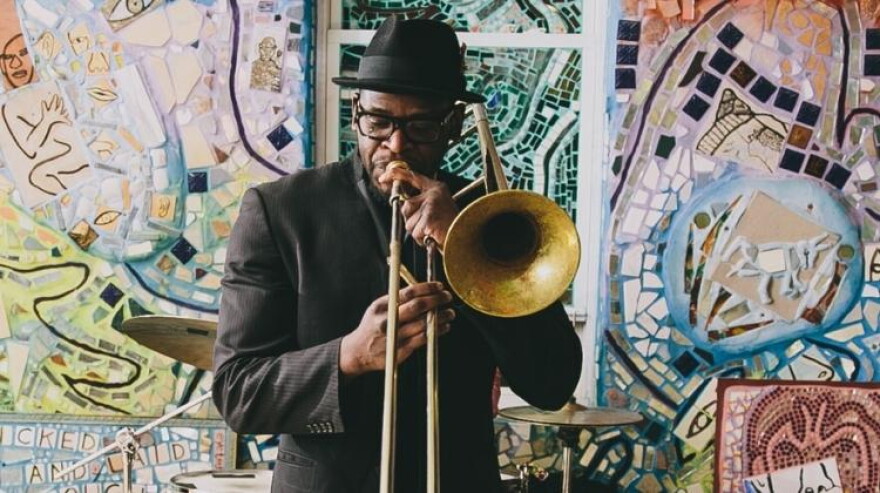 Trombonist Ernest Stuart plays his instrument in front of a mural.
