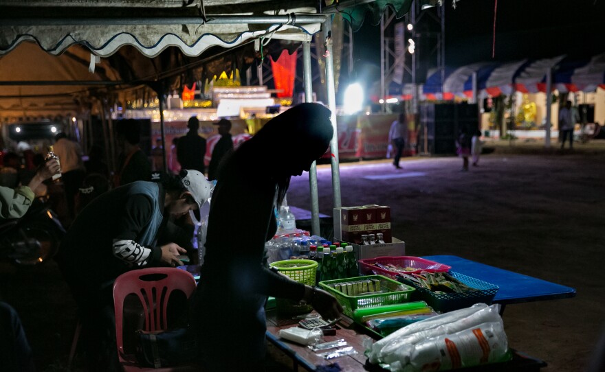 A helps a friend run her stand during a festival in her family's village.