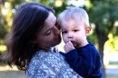 Woman with loving look on her face holds a toddler boy with blond hair in her arms 