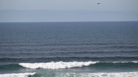 A U.S. Coast Guard helicopter searches the ocean just west of downtown Newport for a twin-engine plane that crashed into the water about 12:45 p.m. Monday.