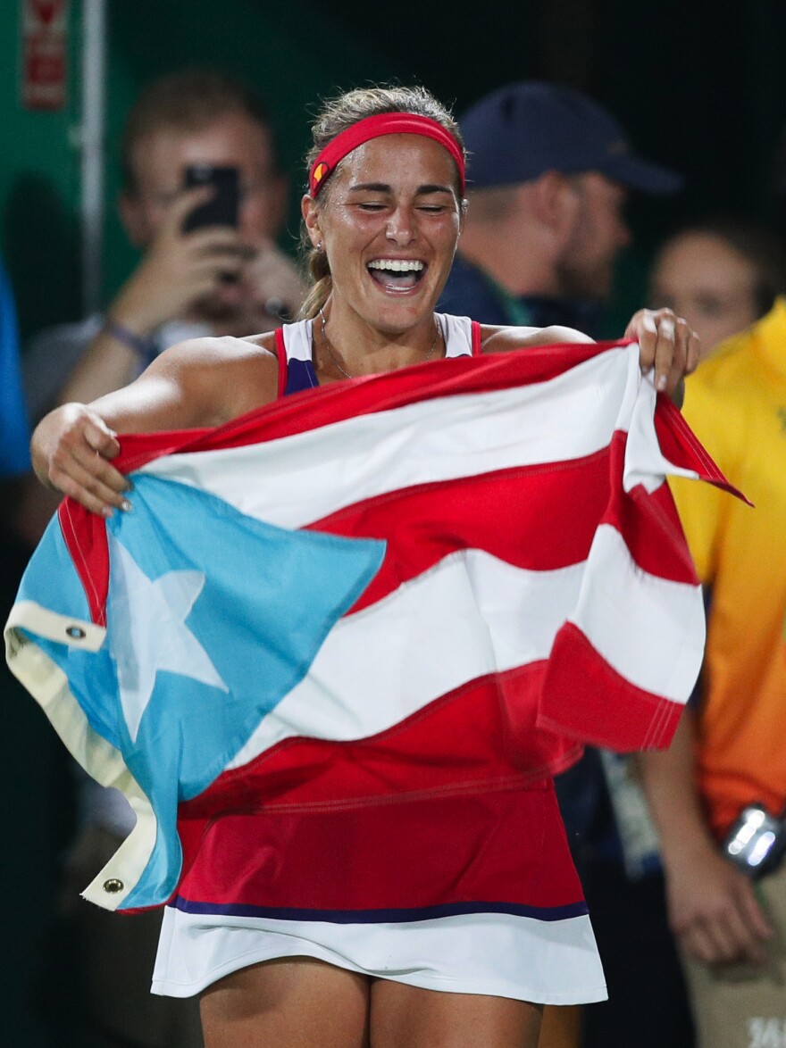 Monica Puig of Puerto Rico celebrates holding her country's flag after winning the gold medal match in the women's tennis competition — Puerto Rico's first-ever Olympic gold medal.