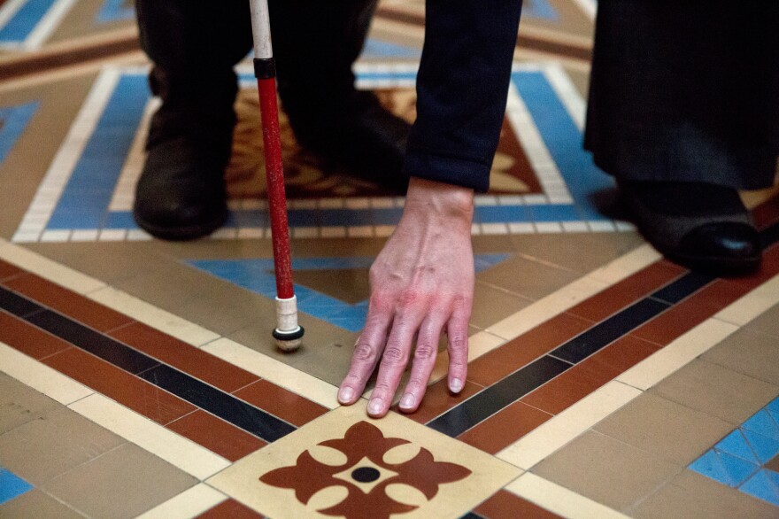 A visitor reaches down to feel the museum floor as a docent describes the corridor in which they are standing.