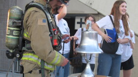 A man in a firefighter uniform rings a silver bell. 