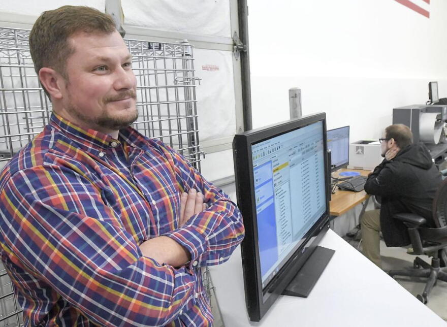 A man crossing his arms next to a computer monitor