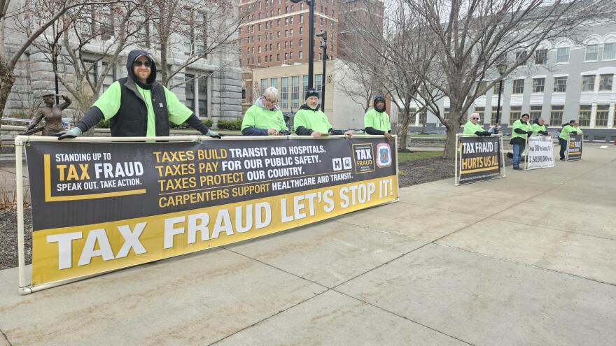 Local carpenters hold signs outside Erie County Hall promoting awareness of construction tax fraud.