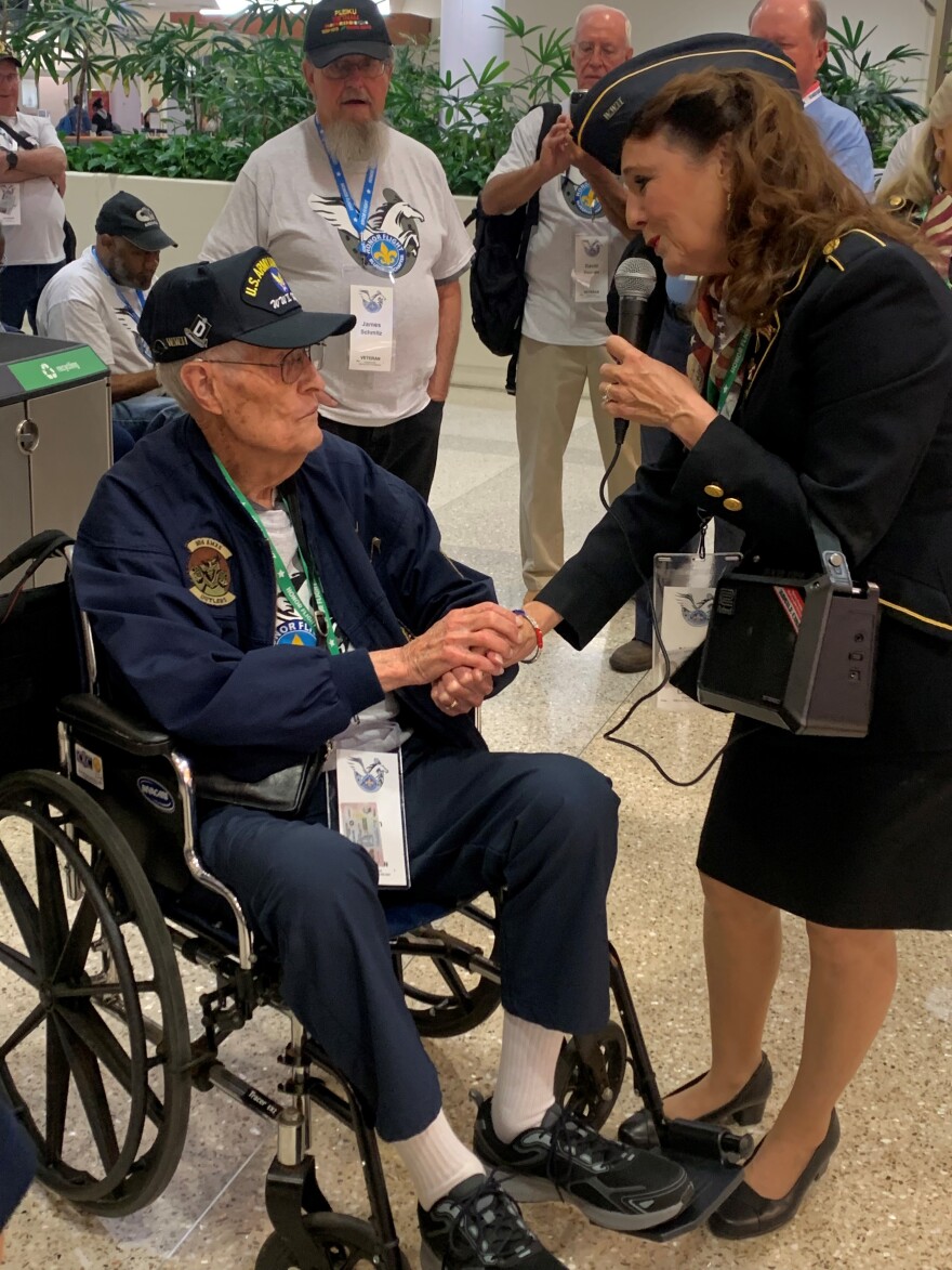 A member of the Ladies for Liberty singing group serenades a WWII veteran at Louisville International Airport before boarding a plane bound for Washington, D.C.