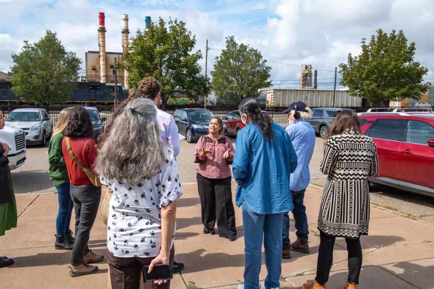 Dearborn, MI., resident and activist Samra'a Luqman (facing camera) speaks to news reporters in the parking lot of a school and community center. In the background is a power plant for nearby industries.