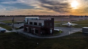 a small airport building with a plane as the sun glows in a cloudy sky
